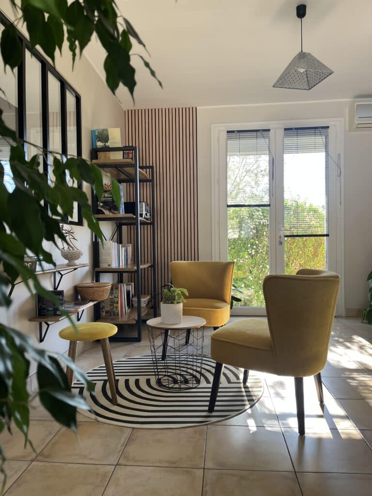 Coin détente lumineux dans une maison avec fauteuils design, tapis graphique et mur en tasseaux bois, projet d’aménagement intérieur à Saint-Christophe-du-Bois